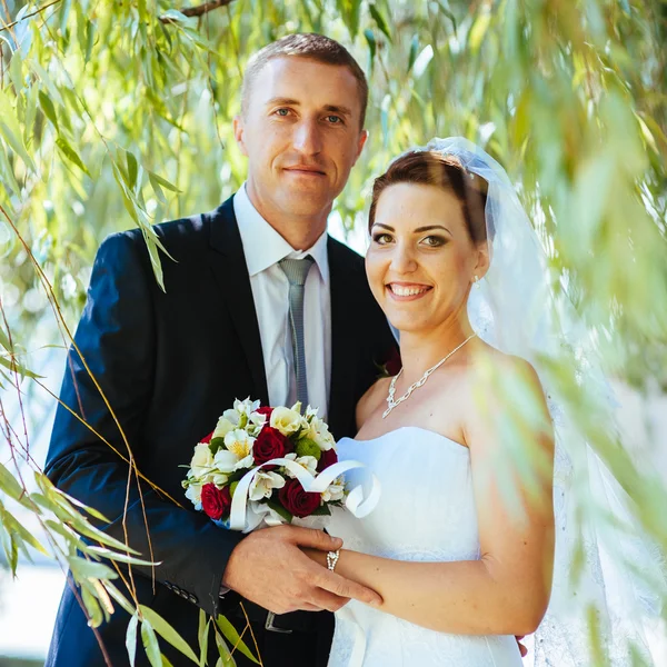 Noiva e noivo no dia do casamento andando ao ar livre na natureza de primavera. Casal nupcial, mulher recém-casada feliz e homem abraçando no parque verde. Casal de amor ao ar livre . — Fotografia de Stock