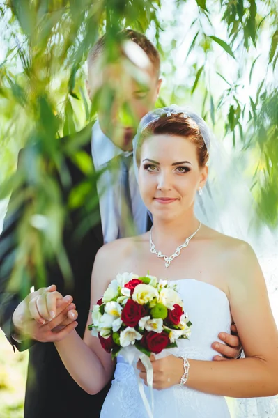 Noiva e noivo no dia do casamento andando ao ar livre na natureza de primavera. Casal nupcial, mulher recém-casada feliz e homem abraçando no parque verde. Casal de amor ao ar livre . — Fotografia de Stock