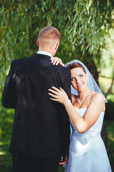 Noiva e noivo no dia do casamento andando ao ar livre na natureza de primavera. Casal nupcial, mulher recém-casada feliz e homem abraçando no parque verde. Casal de amor ao ar livre . — Fotografia de Stock