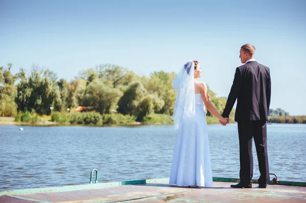 A wedding by the sea. Honeymoon. The bride and groom hugging on the shore of Lake. groom and bride hugging on a green lake. Groom and Bride in a park. wedding dress. Bridal wedding bouquet of flowers. — Stock Photo, Image