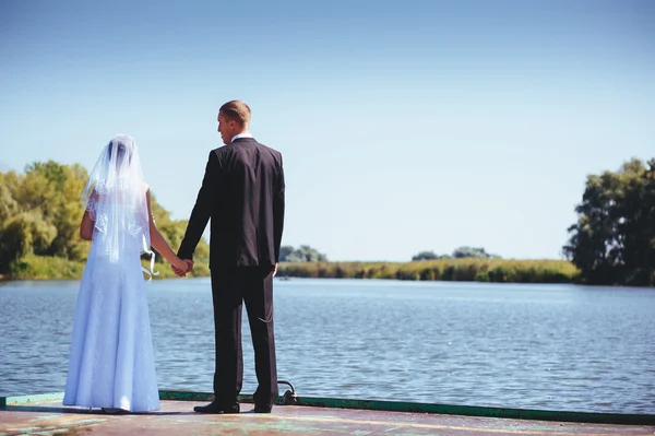 在海边的婚礼。我们的蜜月。新娘和新郎在湖岸的拥抱。新郎和新娘拥抱绿色的湖面上。新郎和新娘在公园里。婚纱礼服。新娘婚礼花束的花朵. — 图库照片