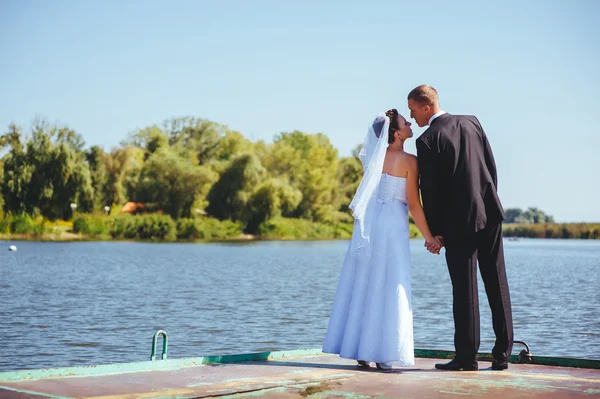 海での結婚式。新婚旅行。湖の岸に抱いて新郎新婦。新郎と新婦の緑湖のハグします。新郎と新婦の公園で。ウェディング ドレス。ブライダル結婚式の花の花束. — ストック写真