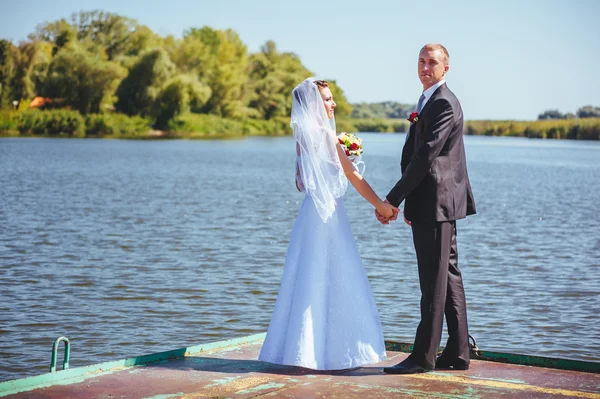 Um casamento à beira-mar. Lua-de-mel. A noiva e o noivo abraçados na margem do lago. noivo e noiva abraçando em um lago verde. O noivo e a noiva num parque. Vestido de noiva. Buquê de casamento nupcial de flores . — Fotografia de Stock