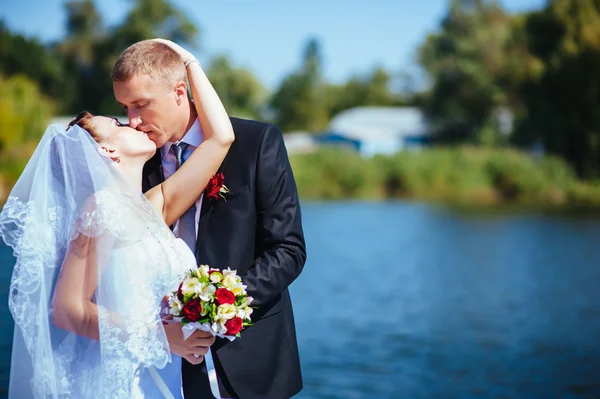 Een bruiloft door de zee. Huwelijksreis. De bruid en bruidegom knuffelen op de oever van het meer. bruid en bruidegom knuffelen op een groen meer. Bruid en bruidegom in een park. trouwjurk. Bruids bruiloft boeket van bloemen. — Stockfoto