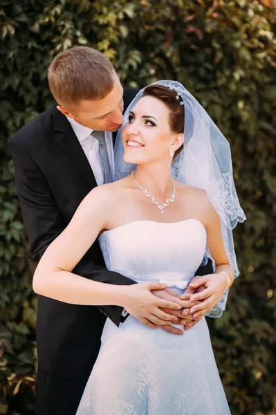 Novia y novio en el día de la boda caminando al aire libre en la naturaleza de primavera. Pareja nupcial, feliz mujer recién casada y hombre abrazándose en el parque verde. Amar pareja de boda al aire libre . — Foto de Stock