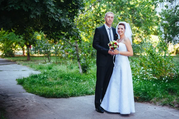 Novia y novio en el día de la boda caminando al aire libre en la naturaleza de primavera. Pareja nupcial, feliz mujer recién casada y hombre abrazándose en el parque verde. Amar pareja de boda al aire libre . —  Fotos de Stock