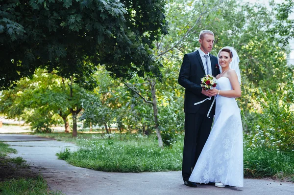 Noiva e noivo no dia do casamento andando ao ar livre na natureza de primavera. Casal nupcial, mulher recém-casada feliz e homem abraçando no parque verde. Casal de amor ao ar livre . — Fotografia de Stock