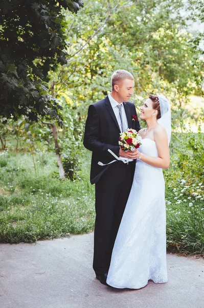 Novia y novio en el día de la boda caminando al aire libre en la naturaleza de primavera. Pareja nupcial, feliz mujer recién casada y hombre abrazándose en el parque verde. Amar pareja de boda al aire libre . —  Fotos de Stock