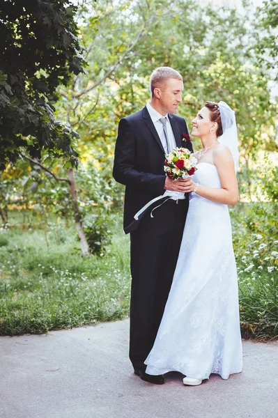 Novia y novio en el día de la boda caminando al aire libre en la naturaleza de primavera. Pareja nupcial, feliz mujer recién casada y hombre abrazándose en el parque verde. Amar pareja de boda al aire libre . —  Fotos de Stock