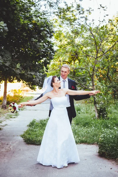 Noiva e noivo no dia do casamento andando ao ar livre na natureza de primavera. Casal nupcial, mulher recém-casada feliz e homem abraçando no parque verde. Casal de amor ao ar livre . — Fotografia de Stock