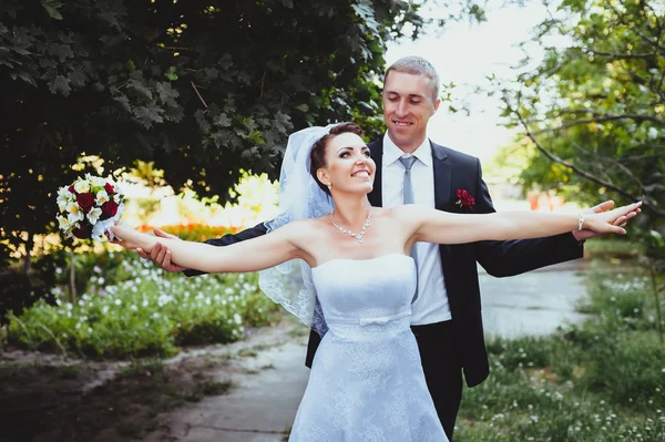 Noiva e noivo no dia do casamento andando ao ar livre na natureza de primavera. Casal nupcial, mulher recém-casada feliz e homem abraçando no parque verde. Casal de amor ao ar livre . — Fotografia de Stock