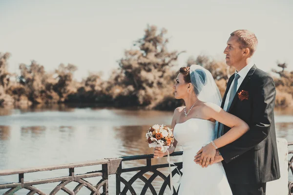 Een bruiloft door de zee. Huwelijksreis. De bruid en bruidegom knuffelen op de oever van het meer. bruid en bruidegom knuffelen op een groen meer. Bruid en bruidegom in een park. trouwjurk. Bruids bruiloft boeket van bloemen. — Stockfoto