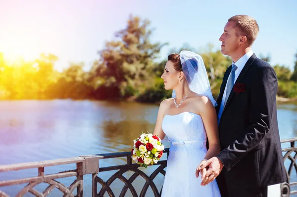 Un mariage près de la mer. Lune de miel. Les mariés se câlinent sur la rive du lac. marié et mariée étreignant sur un lac vert. Groom and Bride dans un parc. robe de mariée. Bouquet de mariage nuptial de fleurs . — Photo