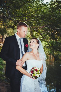 Deniz kenarında bir düğün. Balayı. Gelin ve damat Gölü kıyısına sarılma. damat ve gelin yeşil bir gölde sarılma. Damat ve gelin bir parkta. gelinlik. Gelin düğün buket çiçek.