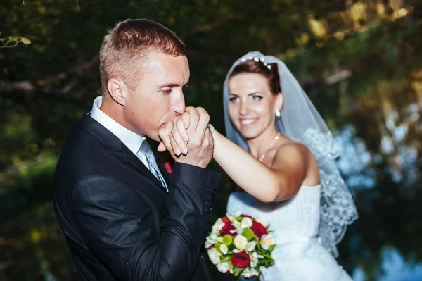 Eine Hochzeit am Meer. Flitterwochen. das Brautpaar, das sich am Seeufer umarmt. Bräutigam und Braut umarmen sich auf einem grünen See. Bräutigam und Braut in einem Park. Brautkleid. Brautstrauß aus Blumen. — Stockfoto