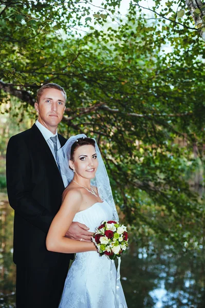 Un mariage près de la mer. Lune de miel. Les mariés se câlinent sur la rive du lac. marié et mariée étreignant sur un lac vert. Groom and Bride dans un parc. robe de mariée. Bouquet de mariage nuptial de fleurs . — Photo