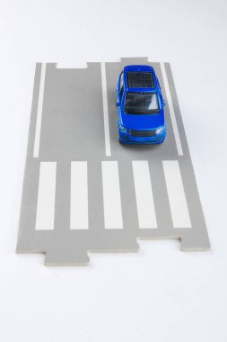 Yolda mavi bir araba yaya geçidinin önünde duruyor.