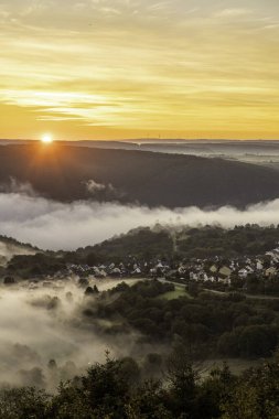 Güneş Bad Salzig yakınlarındaki Rhine Nehri 'nin üzerinden yükselirken gün doğumu gökyüzünü sıcak renklerle boyar. Vadilerden sis yükselir ve sabahın erken saatlerinde dingin bir atmosfer yaratır..