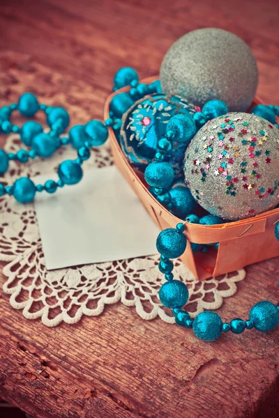 christmas blue silver ornaments beaded necklace and balls in wooden basket with empty paper card on wooden table