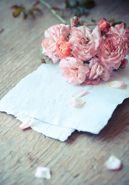 Roze rozen met papieren op houten tafel — Stockfoto