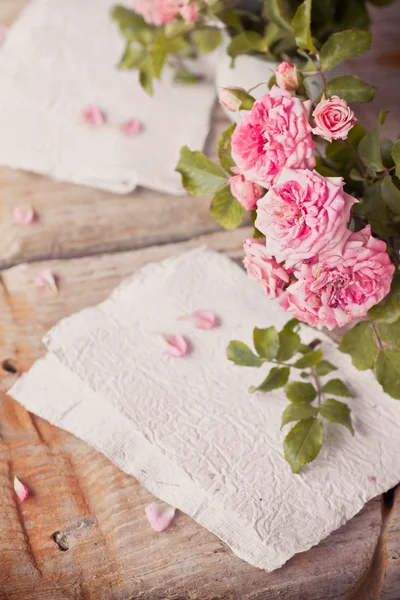 Roze rozen met papieren op houten tafel — Stockfoto