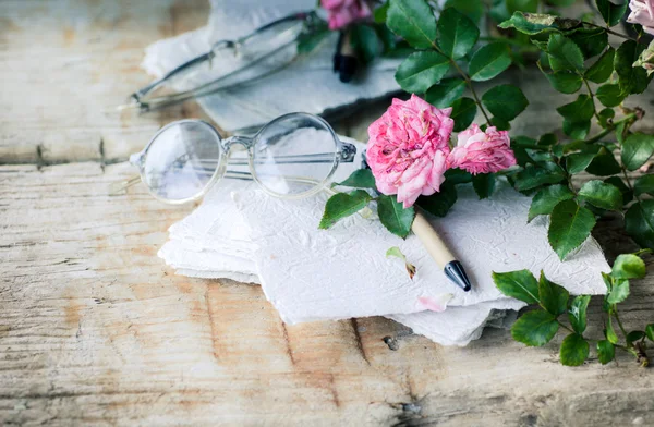 Pink roses with glasses on wooden table — Stock Photo, Image