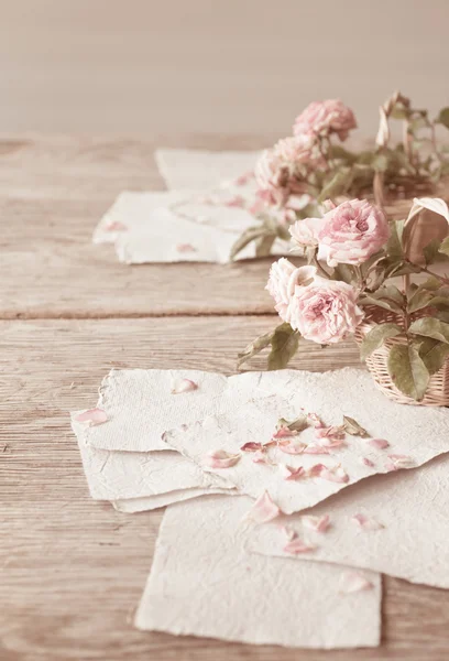 Roze rozen met papieren op houten tafel — Stockfoto