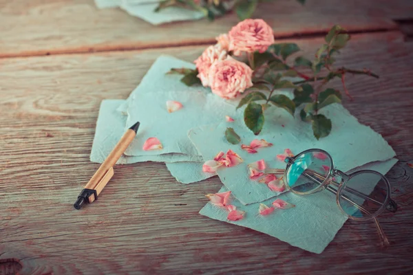 Pink roses with glasses on wooden table — Stock Photo, Image