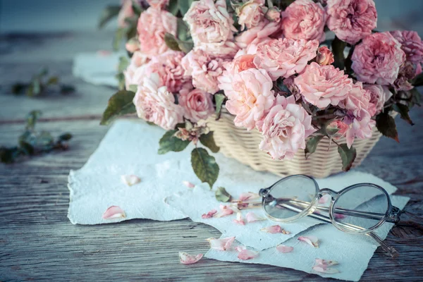 Roze rozen met bril op houten tafel — Stockfoto