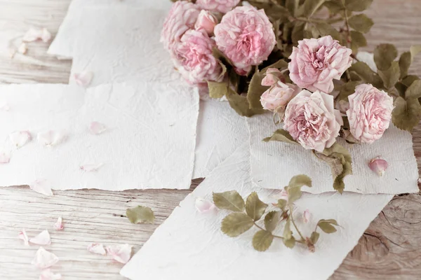 Rosas cor de rosa com papéis na mesa de madeira — Fotografia de Stock