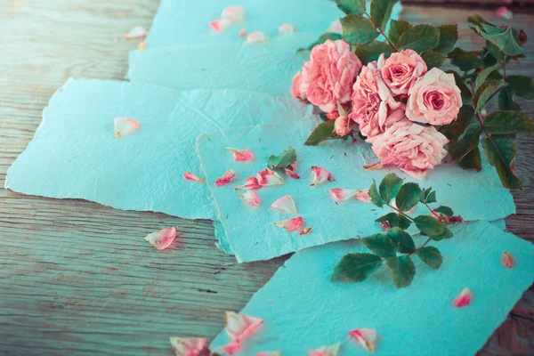 Rosas cor de rosa com papéis na mesa de madeira — Fotografia de Stock