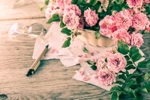 Roze rozen met bril op houten tafel — Stockfoto