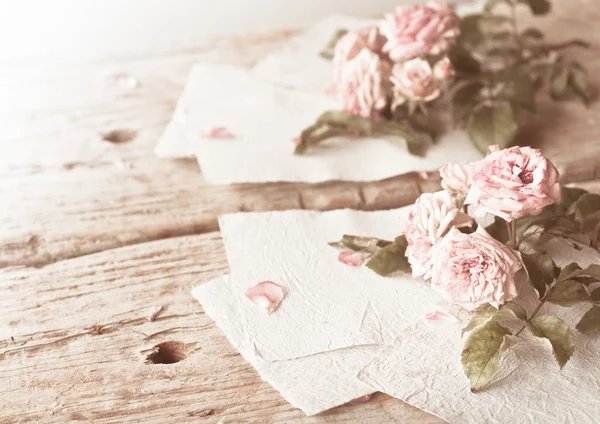 Rosas cor de rosa com papéis na mesa de madeira — Fotografia de Stock