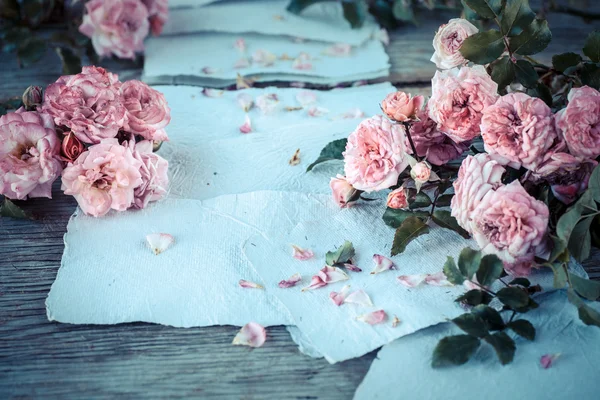 Rosas cor de rosa com papéis na mesa de madeira — Fotografia de Stock