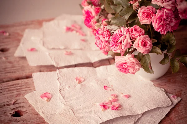 Rosa rosor med papper på träbord — Stockfoto