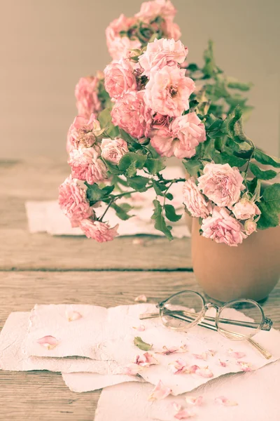 Roze rozen met bril op houten tafel — Stockfoto