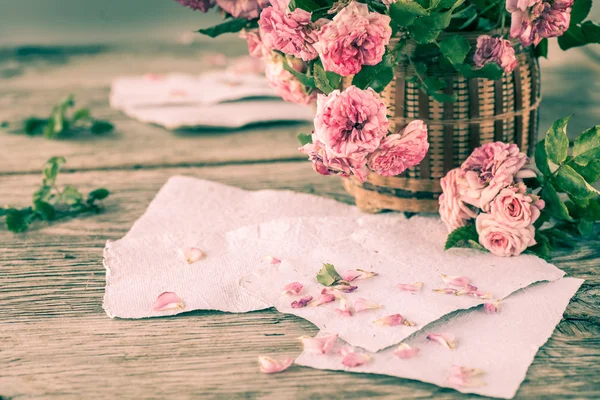 Rosas cor de rosa com papéis na mesa de madeira — Fotografia de Stock