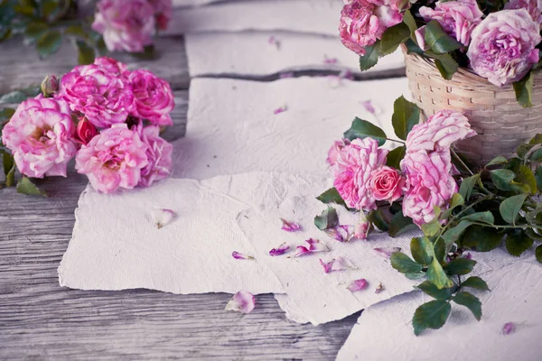 Rosa rosor med papper på träbord — Stockfoto