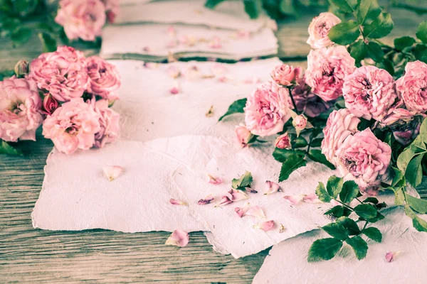 Rosas cor de rosa com papéis na mesa de madeira — Fotografia de Stock