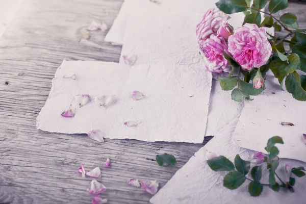 Rosas cor de rosa com papéis na mesa de madeira — Fotografia de Stock