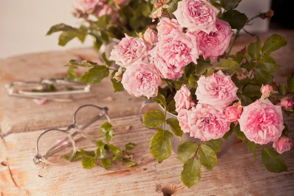 Roses on wooden table with glasses — Stock Photo, Image