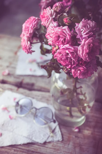 Rosas cor de rosa com óculos na mesa de madeira — Fotografia de Stock