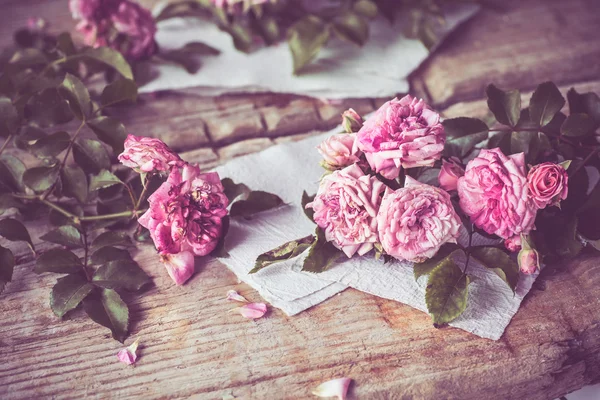 Rosas cor de rosa com papéis na mesa de madeira — Fotografia de Stock