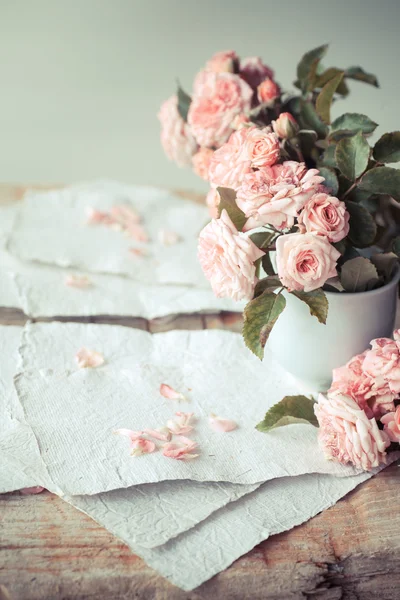 Pink roses with papers on wooden table — Stock Photo, Image