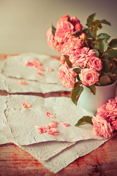 Rosas cor de rosa com papéis na mesa de madeira — Fotografia de Stock
