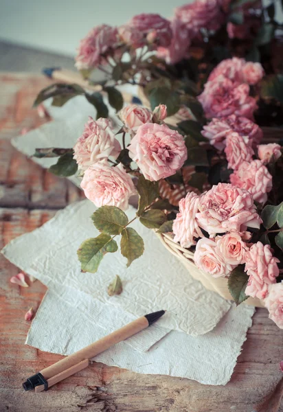 Rosas cor de rosa com papéis na mesa de madeira — Fotografia de Stock