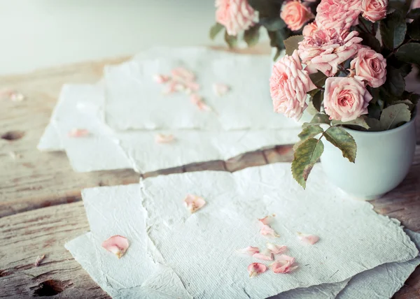 Rosas cor de rosa com papéis na mesa de madeira — Fotografia de Stock