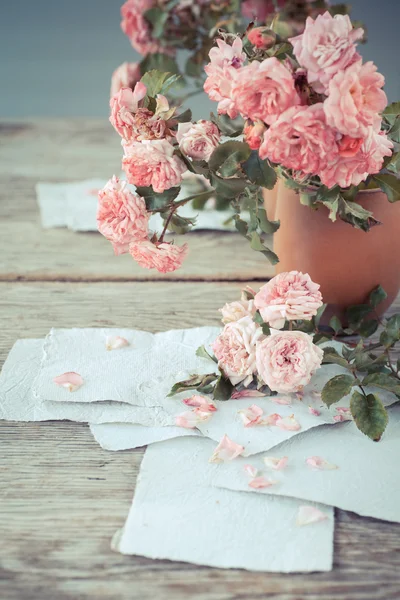 Pink roses with papers on wooden table — Stock Photo, Image