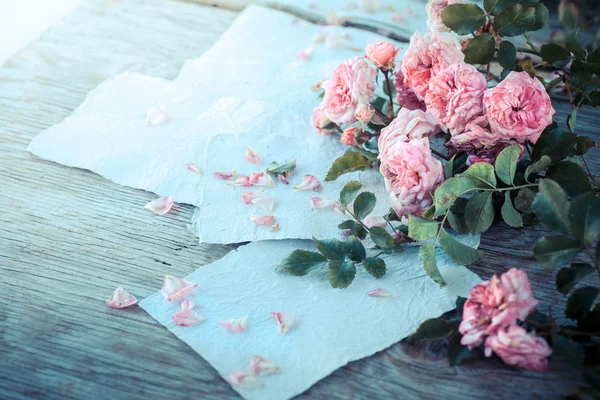 Pink roses with papers on wooden table — Stock Photo, Image