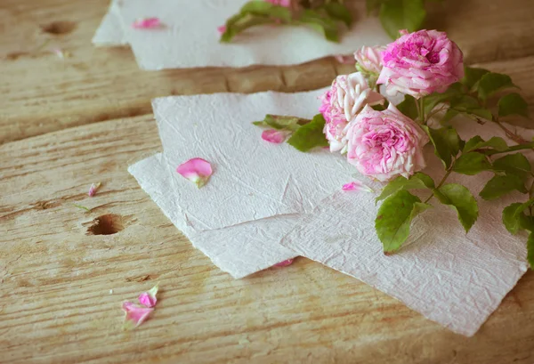 Rosa rosor med papper på träbord — Stockfoto